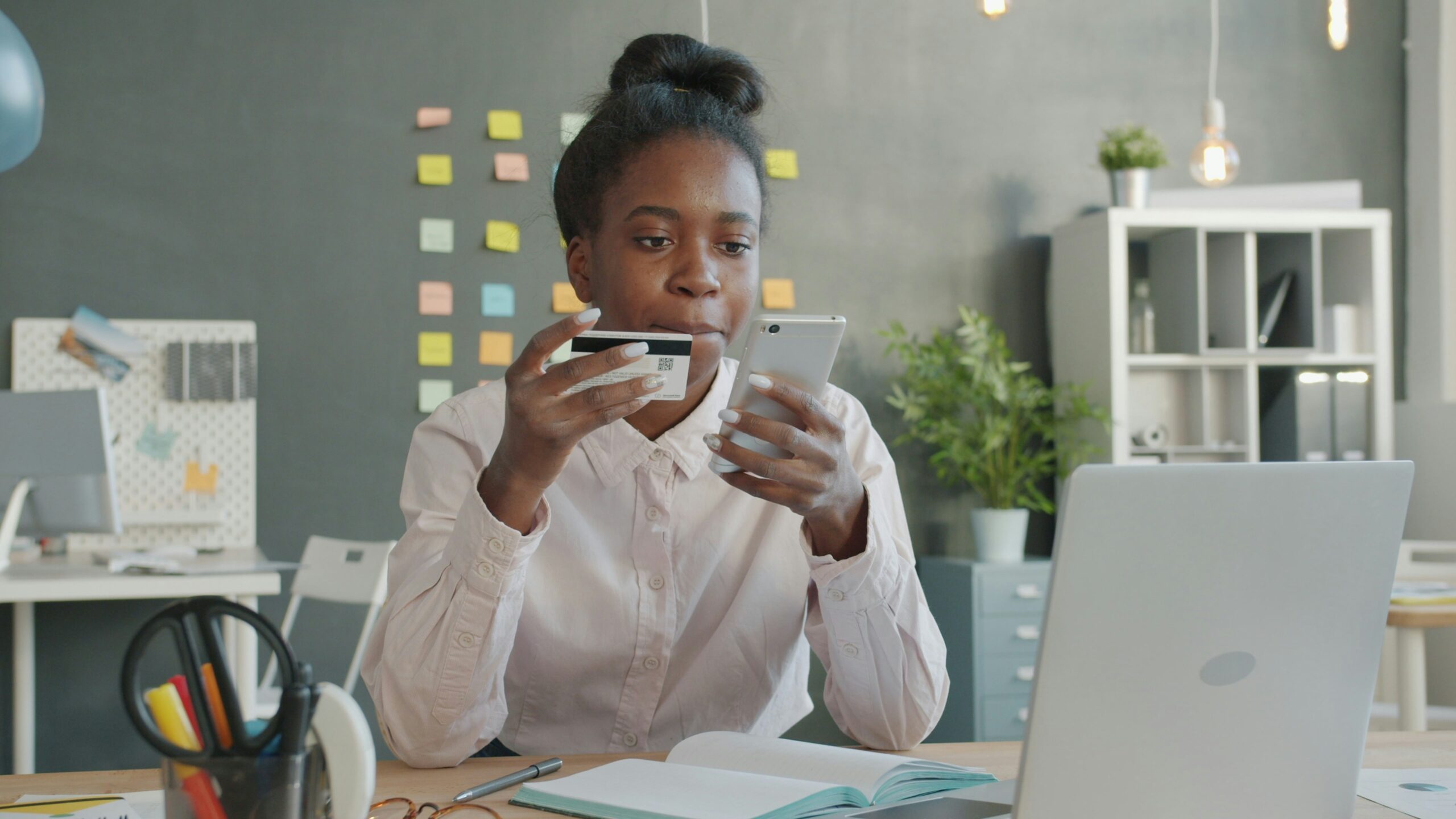 Woman holding credit card and phone at desk