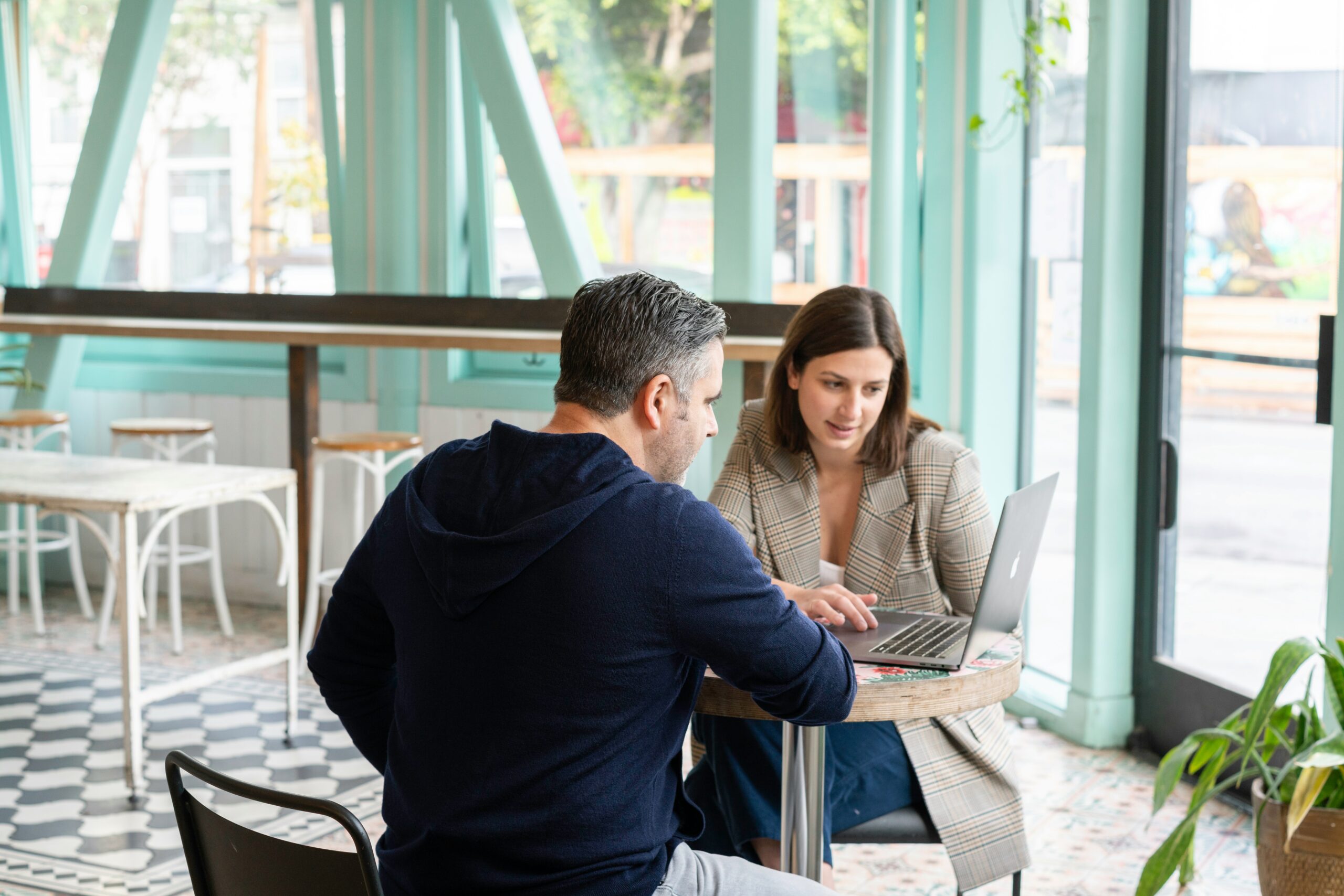 A man and a woman working on a laptop at a cafe table