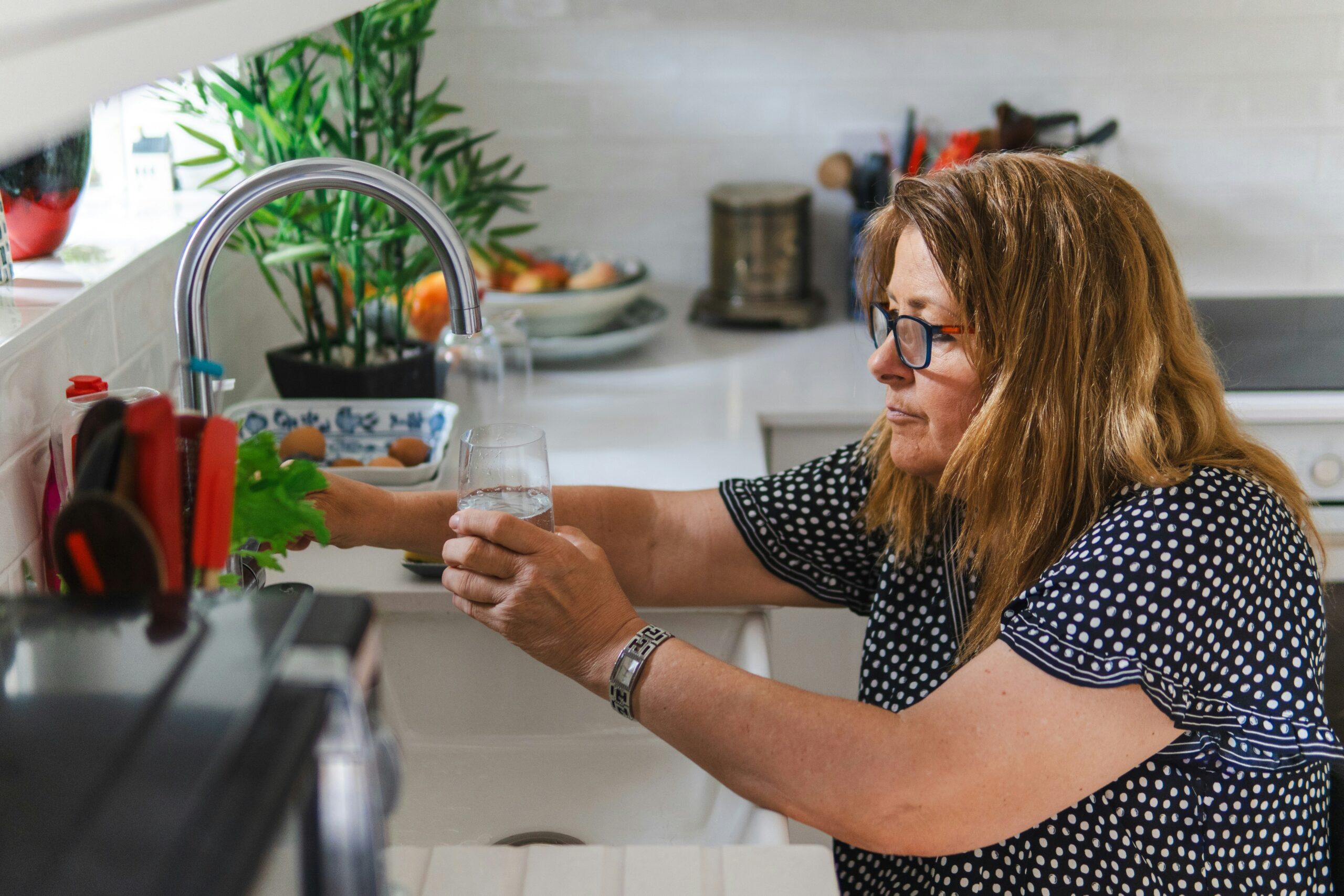 Woman filling a glass with water from a kitchen faucet